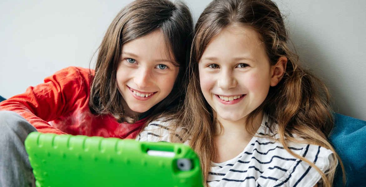 Portrait zwei junger laechelnder Maedchendie vor einem digitalen tablet die an einem tech workshop for kids teilnehmen